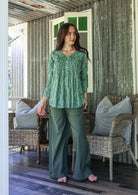 Woman wearing a sage green based floral cotton long sleeve shirt with pin tucks across the back of the bodice, the back of shirt is longer than front