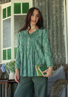 Woman wearing a cotton floral long-sleeve shirt with a V-neckline, standing in a room with decorative elements.