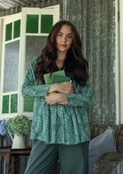 Woman holding a green book in a rustic setting with a window and curtains.