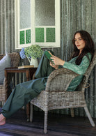 Woman sitting in a wicker chair reading a book in a room with textured walls and a window.