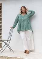 Woman wearing a sage green based floral cotton long sleeve shirt with pin tucks across the back of the bodice, the back of shirt is longer than front