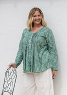 Woman wearing a sage green based cotton floral long sleeve relaxed fit blouse with a V-neckline.