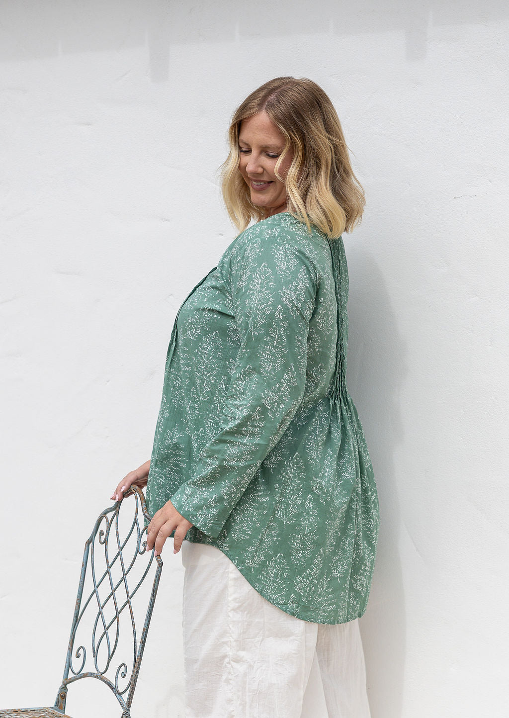 Woman stands side ways wearing a cotton long sleeve shirt that is longer at the back, paired with plain cotton pants