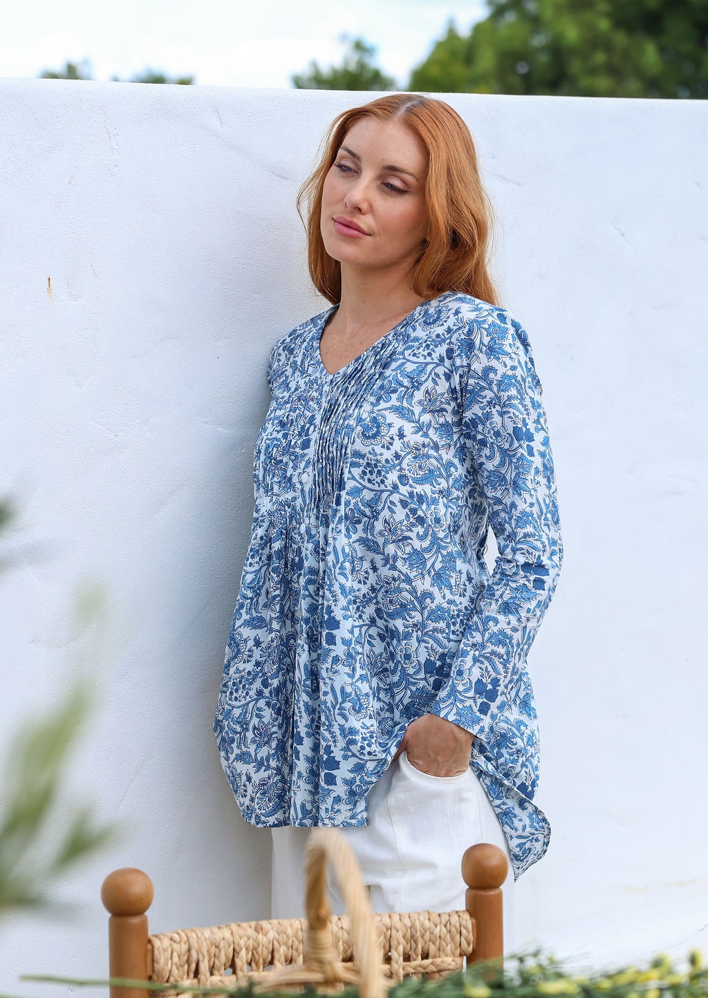 Woman wearing a white based blue floral cotton long sleeve shirt with pin tucks across the back of the bodice, the back of shirt is longer than front
