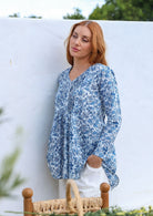Woman wearing a white based blue floral cotton long sleeve shirt with pin tucks across the back of the bodice, the back of shirt is longer than front