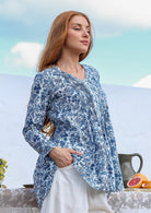 woman stands sideways wearing a 100% cotton  white based blue floral print long-sleeve top. 
