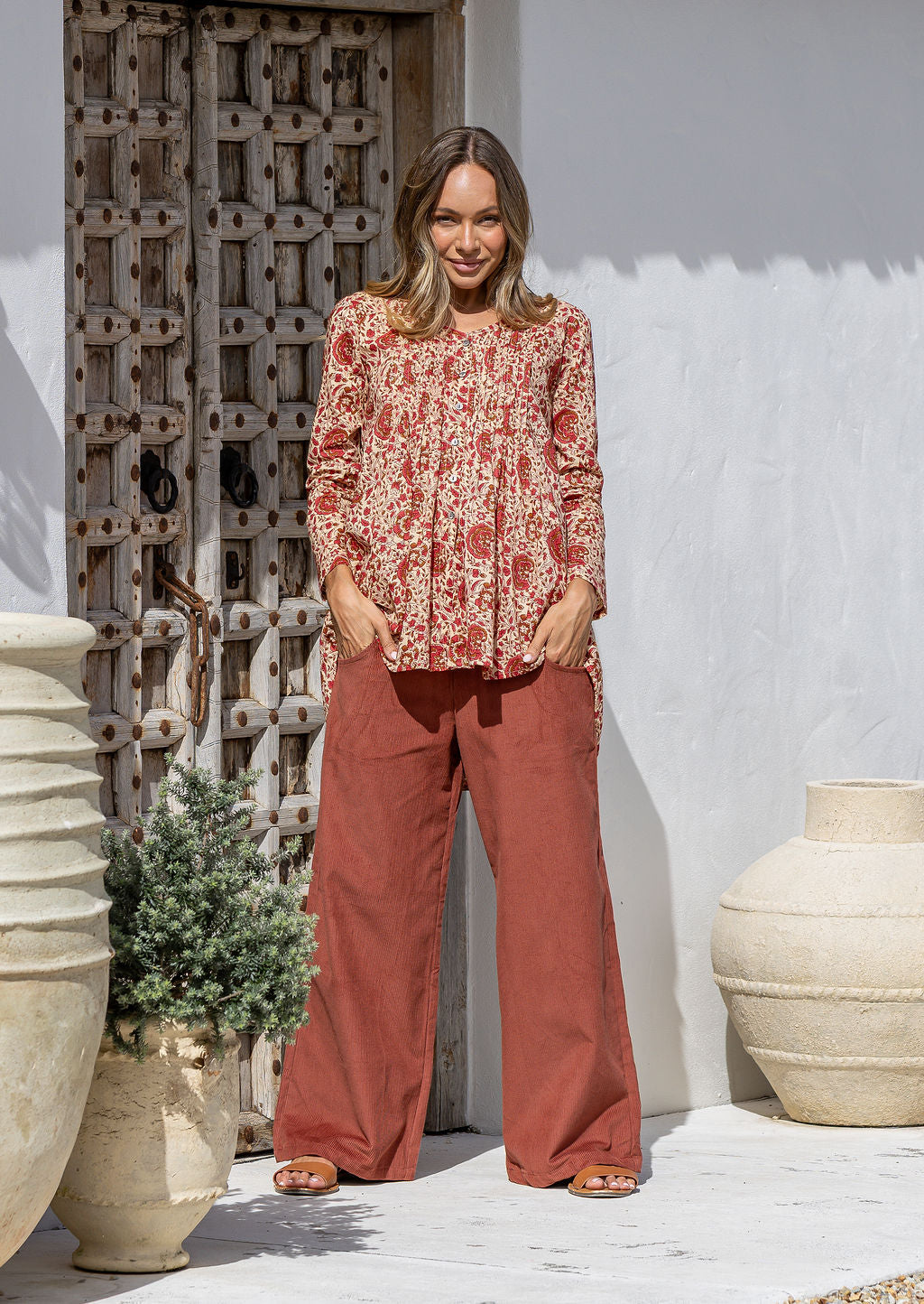 Woman wearing a cream based floral cotton long sleeve shirt with pin tucks across the back of the bodice, the back of shirt is longer than front