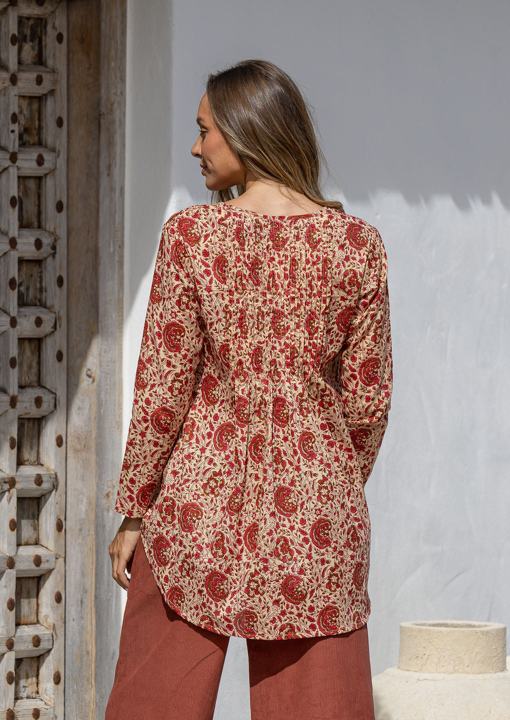 Woman standing backwards wearing a cotton floral long-sleeve shirt with a V-neckline, standing outdoor