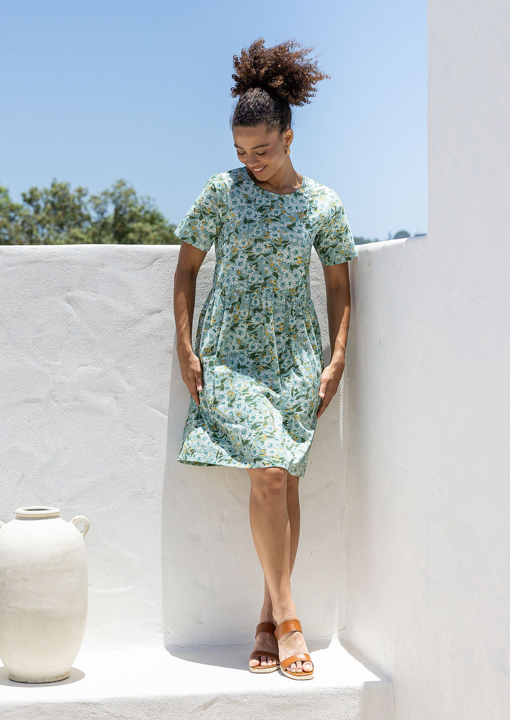 Woman wearing a relaxed fit, above knee length cotton dress with sage green based floral print.