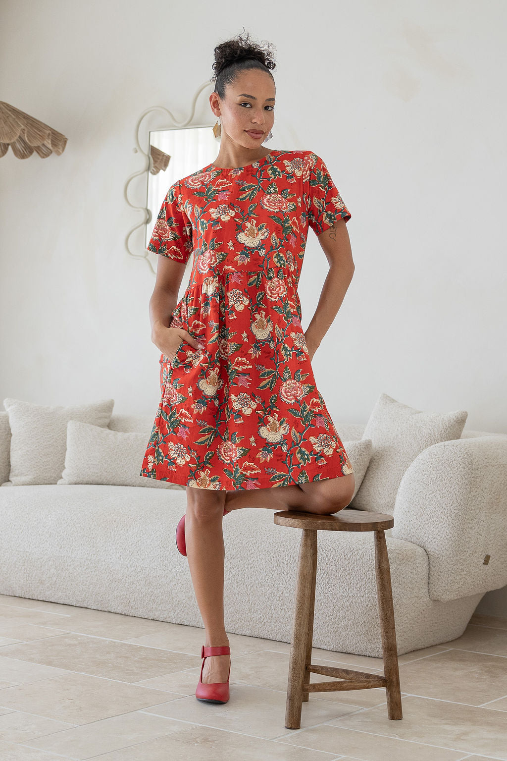 Woman poses with both hands in pockets of a 100% cotton relaxed fit dress with round neckline and short sleeves.