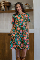 Woman standing with one hand in pocket of a 100% cotton dress in olive green based floral print