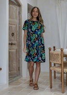 Woman wearing a above knee length floral cotton dress with short sleeves, pockets and round neckline 