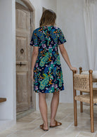 Woman standing backwards wearing a 100% cotton navy blue based floral relaxed fit dress with round neckline and short sleeves.