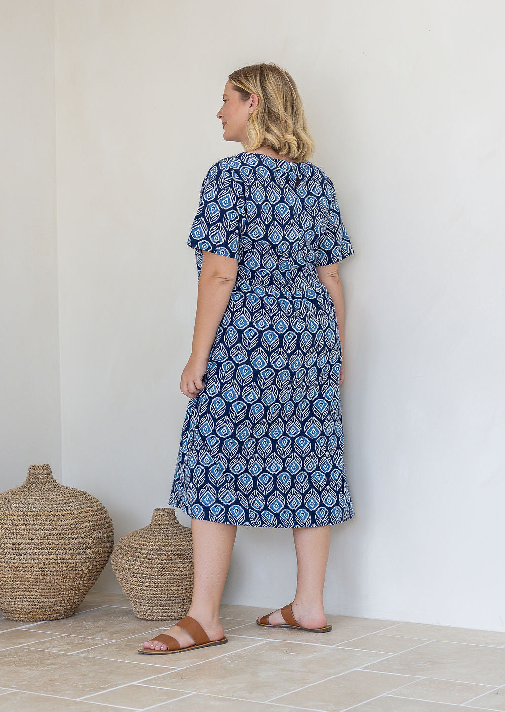 Woman stands backwards wearing a 100% cotton relaxed fit short sleeve dress in navy based floral print. 