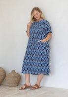 Model poses in relaxed fit cotton midi length dress with short sleeves and high round neckline with one hand in pocket