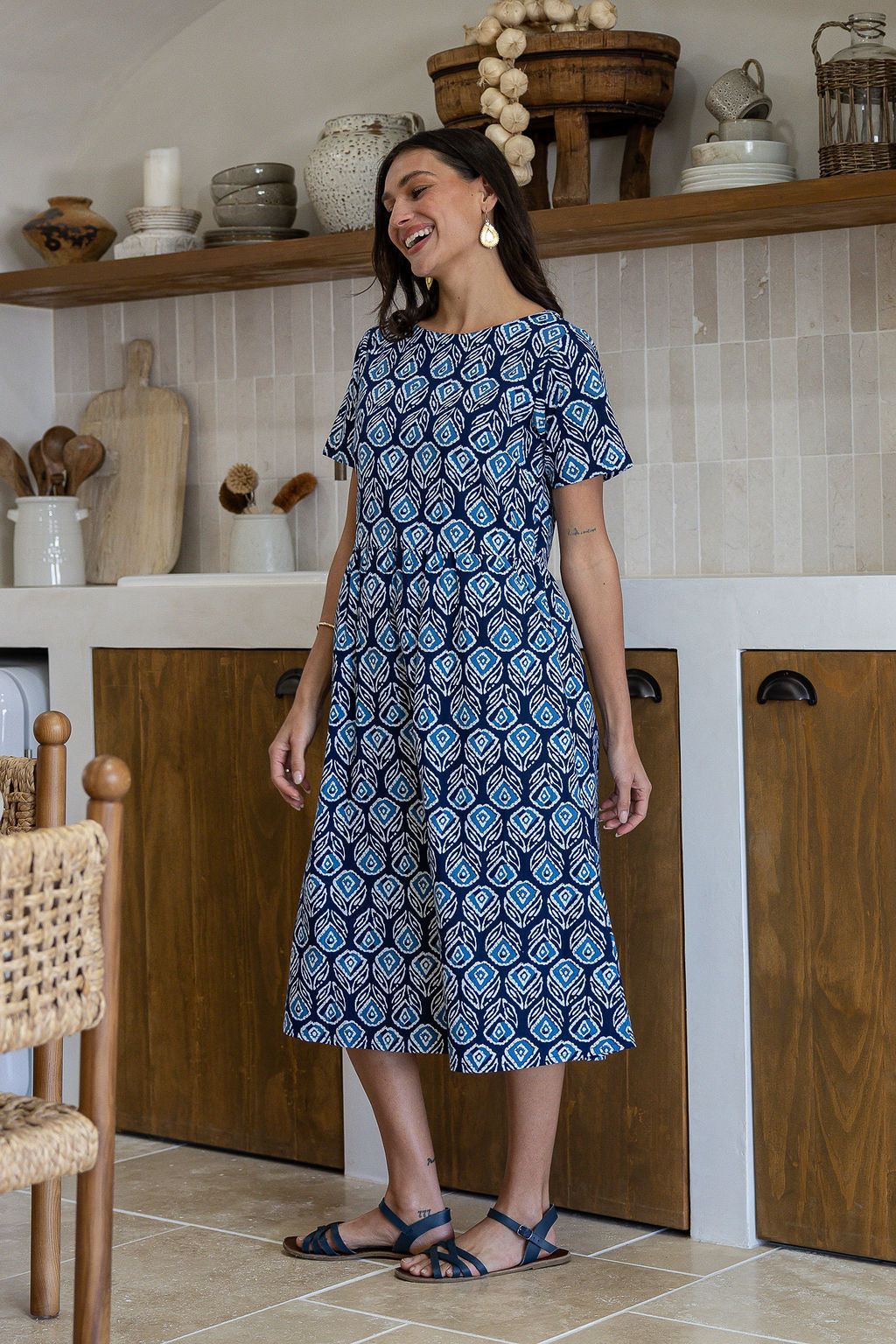 Woman wearing a 100% cotton relaxed fit dress in navy based floral print with round neckline standing in a kitchen