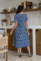 Woman stands backwards wearing a 100% cotton relaxed fit short sleeve dress in navy based floral print. 