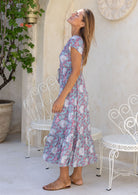 Model looking up over her shoulder wearing 100 percent rayon maxi dress in blue based floral print