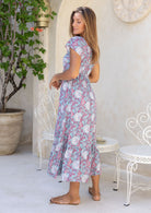 Model standing infront of white wall wearing 100 percent rayon maxi dress in blue based floral print