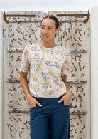 Woman wearing a 100 percent cotton, neutral based floral loose cut top with high round neckline and short sleeves