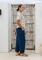 Woman in neutral based floral boxy style cotton top with short sleeves, round neckline and plain blue pants.