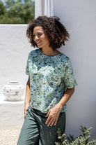 Woman wearing a 100 percent cotton, sage green based floral loose cut top with high round neckline and short sleeves