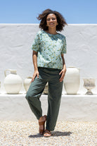 Woman in sage green based floral cotton top with short sleeves, round neckline and plain green pants.