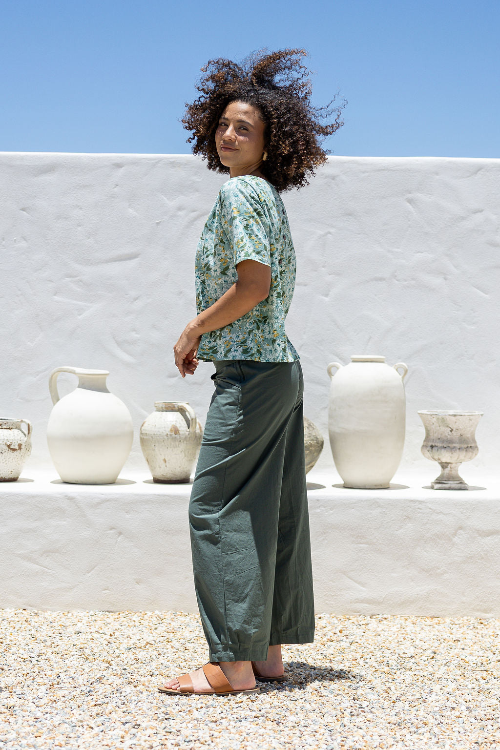 Woman stands sideways wearing a 100 percent cotton loose cut blouse in sage green based floral print and plain green pant. 