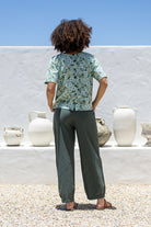 Woman stands backwards wearing a 100 percent cotton loose cut blouse in sage green based floral print and plain green pant. 