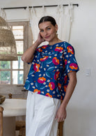 Woman wearing a royal blue based floral printed cotton short sleeved top and white plain pants. 