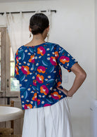 Woman standing backwards wearing a relaxed n fit royal blue based printed cotton top with decorative buttons down the centre back