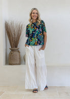 Woman wearing a blue based floral print  cotton short sleeved top and white plain pants in a outdoor setting.