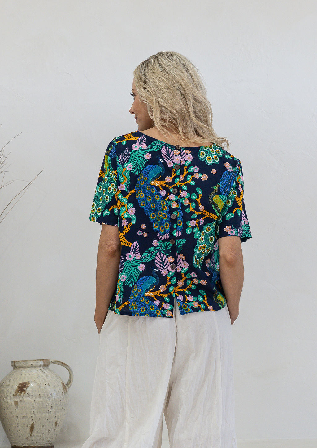 Back view of woman wearing relaxed fit navy based floral print cotton top with decorative buttons down the centre back