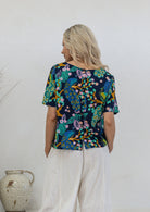 Back view of woman wearing relaxed fit navy based floral print cotton top with decorative buttons down the centre back
