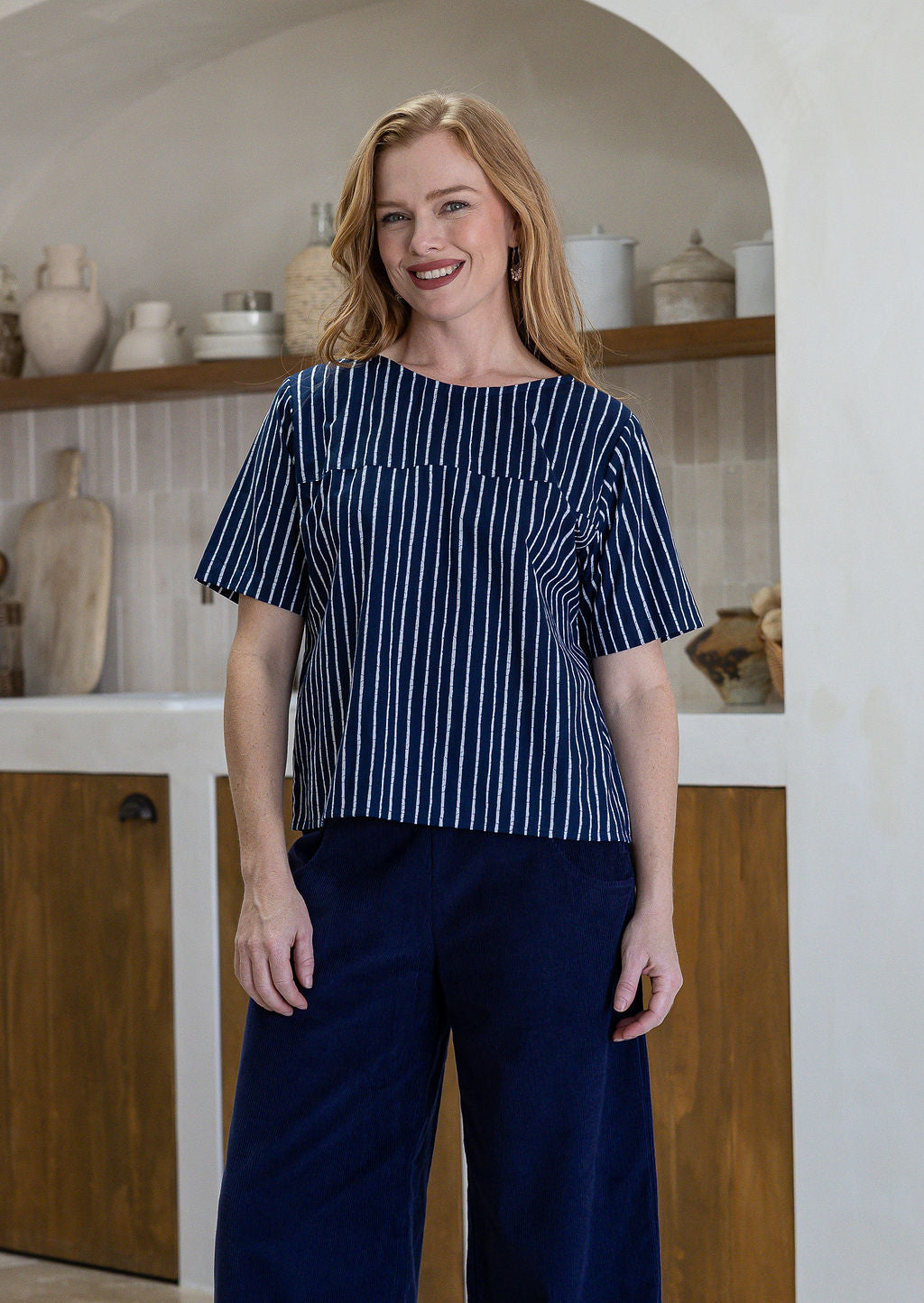 Woman wearing a blue and white striped cotton top and dark blue pants in a kitchen setting.