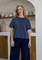 Woman wearing a blue and white striped cotton top and dark blue pants in a kitchen setting.