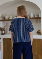 Back view of woman wearing relaxed fit navy and white striped cotton top with decorative buttons down the centre back