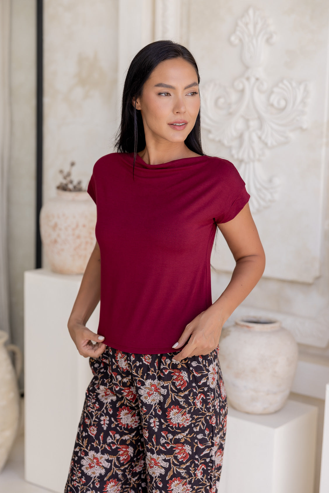 Woman wearing a wide neck mod maroon 100% rayon boat neck top paired with floral cotton pants.
