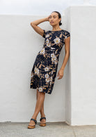 Model wears a knee length A line dress with cap sleeves in black based floral print