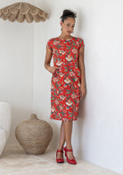 Model with one hand in pocket wears a knee length A line dress with cap sleeves in red based floral print