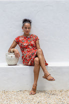 woman wearing bright red cotton floral retro style dress sitting on white wall 