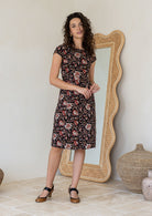 Woman wearing a simple knee length cotton dress with round neckline, short cap sleeves, pockets and a slight A-line skirt.