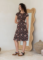Model posing in a black floral print shirt style 100% cotton dress with cap sleeves 