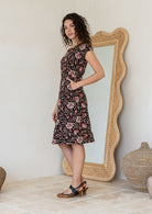 Model stands sideways with hands in pocket of a Indian traditional print short sleeve sundress.