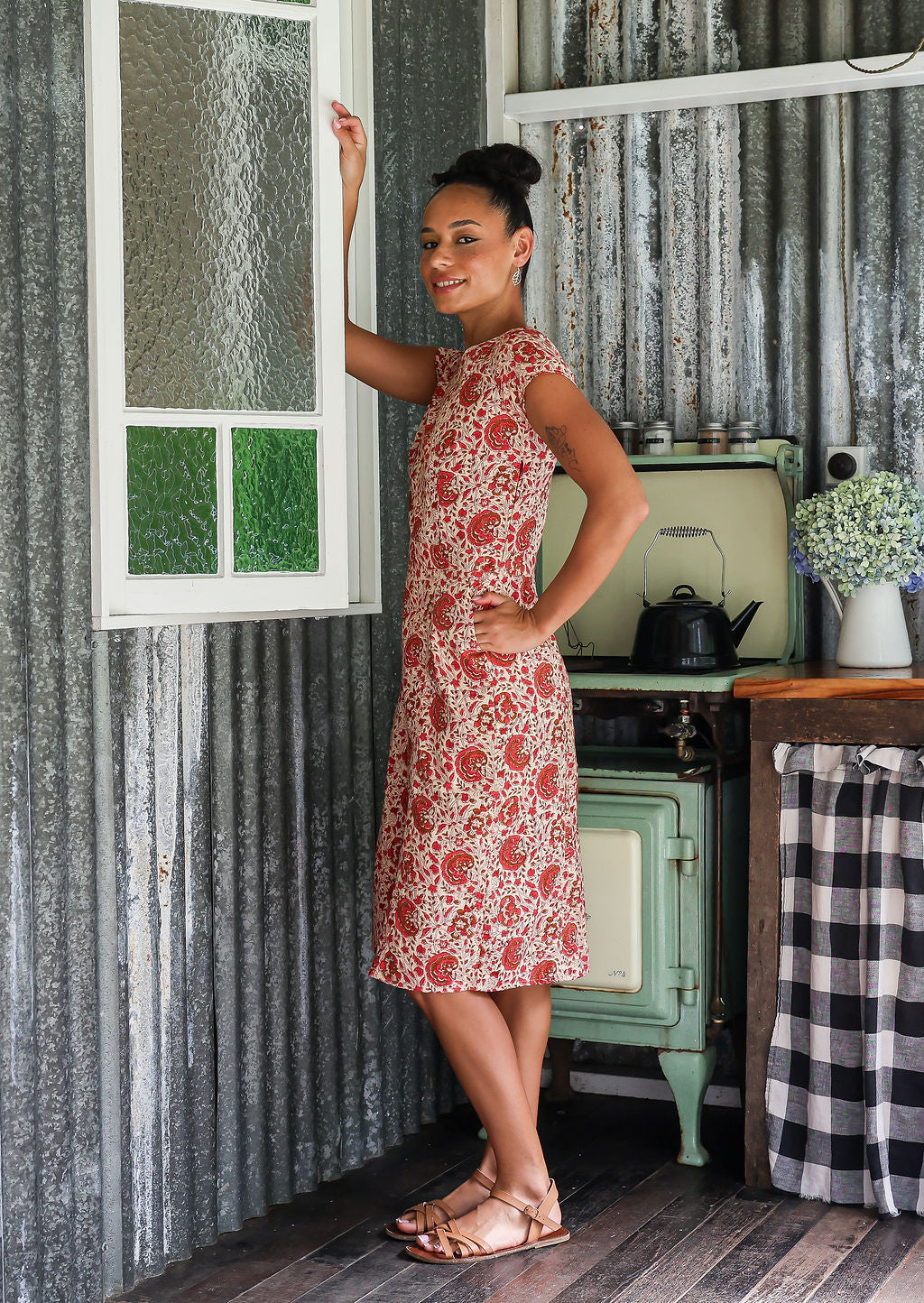 Woman stands sideways wears a 100% cotton, knee-length A-line floral dress.