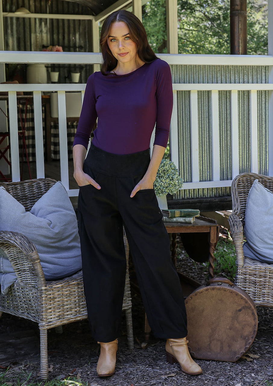 Woman standing in front of a porch wearing black cotton corduroy pants with hands in pockets