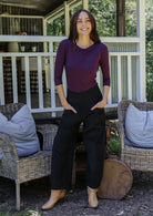 Woman posing in black cotton corduroy pants with hands in pockets, paired with a purple top and tan boots
