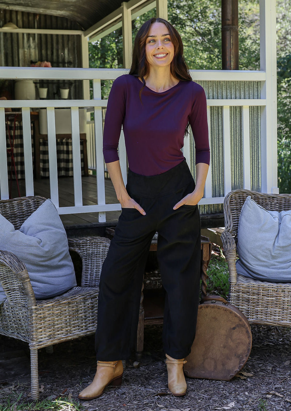 Woman posing in black cotton corduroy pants with hands in pockets, paired with a purple top and tan boots