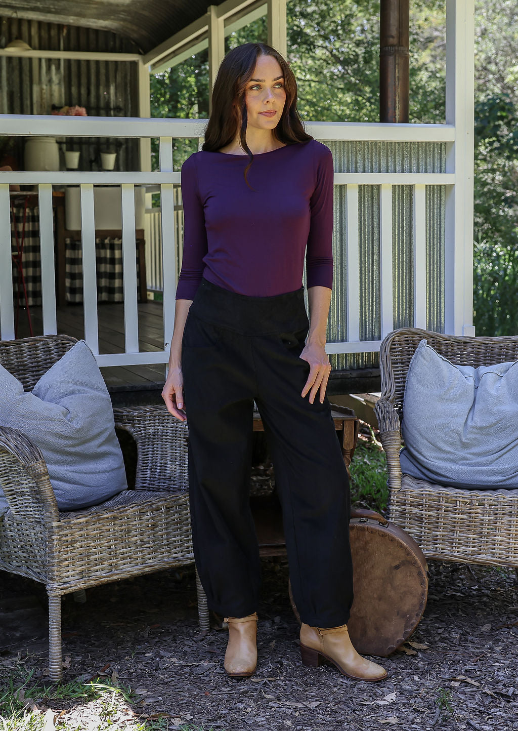Woman standing in front of porch wearing black cotton corduroy pants paired with a purple top and tan boots