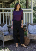 Woman standing in front of porch wearing black cotton corduroy pants paired with a purple top and tan boots